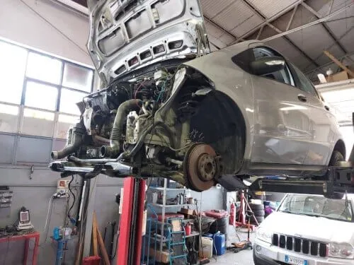 Un meccanico che lavora su un'auto, con una chiave inglese in mano e una parte dell'auto aperta.